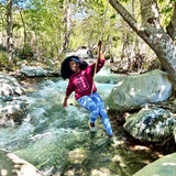‘Dami in Tribal Marks No Wahala Ankara print crewneck and leggings while swinging over a stream in a forested area
