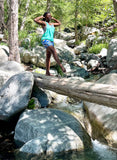 Woman wearing The Wrapper Ankara print sports bra set standing on log over rocky creek in the forest.