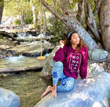 woman wearing Tribal Marks No Wahala Crewneck sweatshirt sitting on a rock at a creek