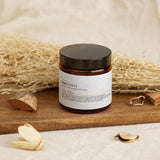 Tribal Marks SheaCrafted magnesium lotion in an amber jar on a wooden tray with stray in the background