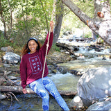 Woman wearing a maroon No Wahala Ankara print Crewneck sweatshirt with over No Wahala Ankara leggings pockets sitting on a swing over a rushing creek
