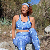 Smiling woman sitting on a rock outdoors with trees in a wild outdoorsy setting wearing No Wahala Ankara print matching set – leggings with pockets styled with matching sports bra.