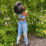 Happy woman wearing a The Wrapper Ankara print athleisure sports bra and pocket leggings set standing in a natural setting with greenery.