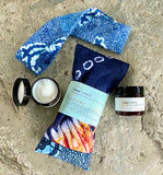 Flatlay of Tribal Marks Ankara Herbal Aromatherapy Eye Pillow bundle with SheaCrafted Magnesium lotions jars and No Wahala Ankara print stretch headband on a rock surface