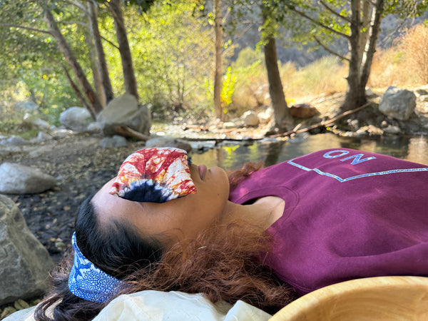 Woman relaxing outdoors by the creek with TribalMarks' Tie-Dye Ankara Aromatherapy Lavender eye pillow, covering her eyes