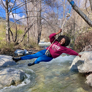 Gleeful 'Dami on a swing over a mountain creek wearing Tribal Marks Beloved Sage Collection Crewneck Sweatshirt saying Love Slays Fear. Repeat.